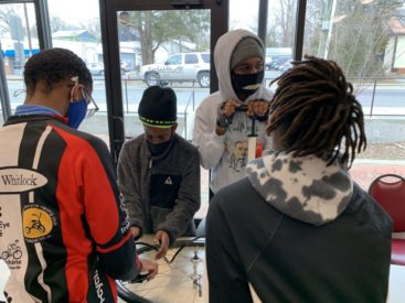 Youth gathered around wheel of bike on table pumping tire